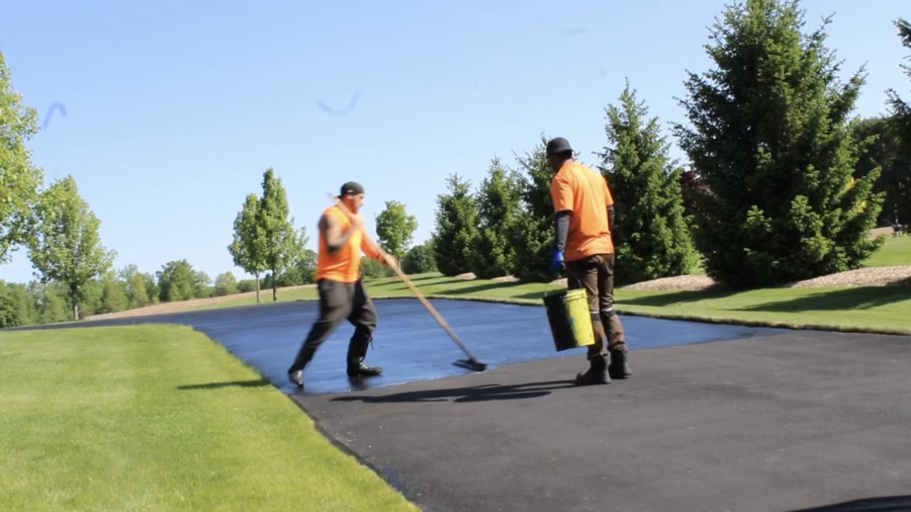 Causyns Construction crew brushing asphalt sealer onto a driveway